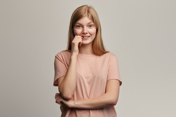 nervous emotional beautiful girl in beige T-shirt feels anxious and surprised, bites nails in puzzlement worries before exams. close up portrait. isolated gray background. emotion concept