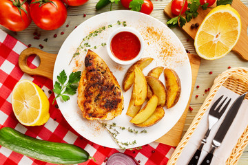 Top view plate of fried chicken with potato at decorated with vegetables wooden table background.