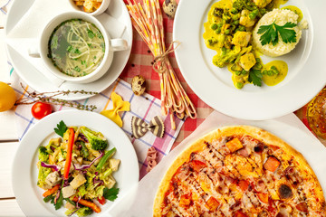 Top view image of italian style business lunch of pizza, soup, steamed vegetables and salad at wooden table background.