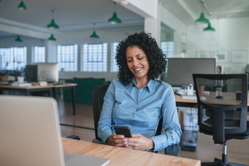 Smiling businesswoman sitting at her desk reading a text message
