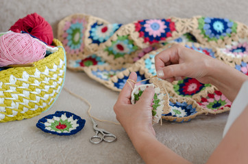 Multicolored plaid squares of crocheted on a cream colored seat and woman is crocheting