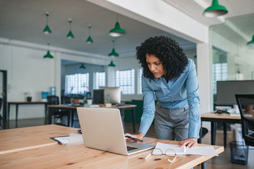 Focused young businesswoman standing at her desk using a laptop