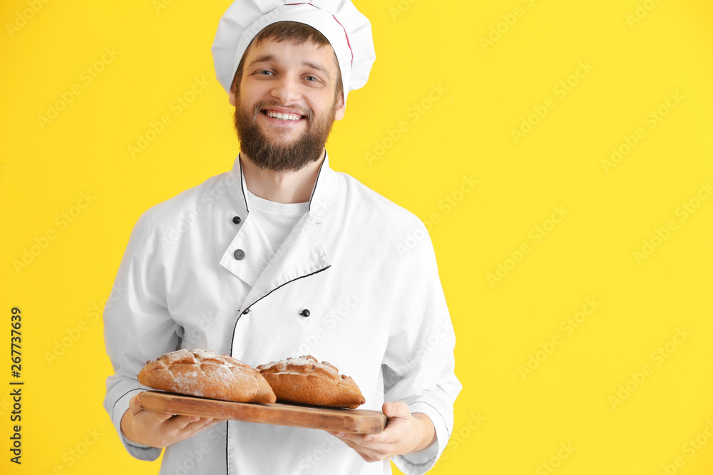 Wall mural Young baker with fresh bread on color background