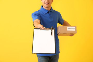 Delivery man with box and clipboard on color background