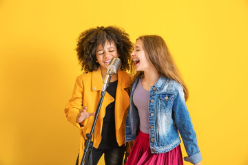 Teenage girls with microphone singing against color background