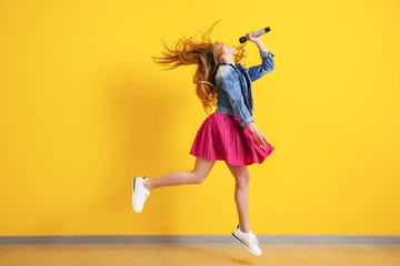 Teenage girl with microphone jumping and singing against color wall