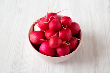 Fresh radishes in a pink bowl over white wooden background, low angle view. Close-up.