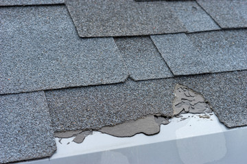 Сloseup view of asphalt shingles roof damage that needs repair.
