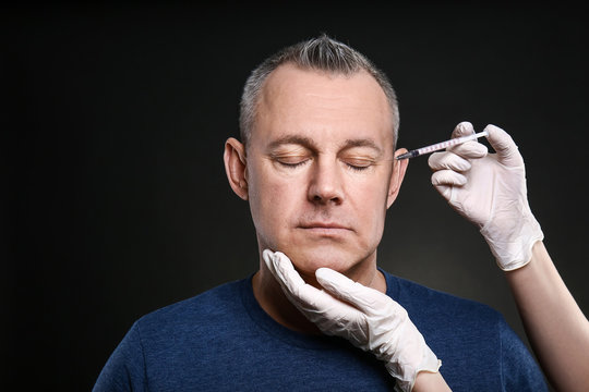 Middle-aged man and hands holding syringe for anti-aging injections on dark background