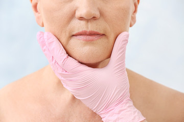 Plastic surgeon touching face of mature woman on light background, closeup