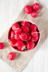 Fresh red radishes in a pink bowl over white wooden background, top view. Flat lay, overhead, from above. Close-up.