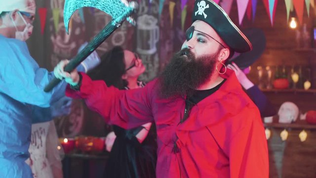 Handsome young man with big beard dressed as a pirate at a halloween party. Authentic looking with a eyeband, jolly roger hat and hook instead of a hand.