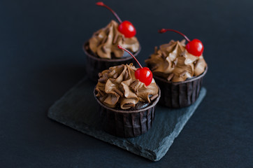 Chocolate cupcakes with chocolate cream decorated with cocktail cherry on black background