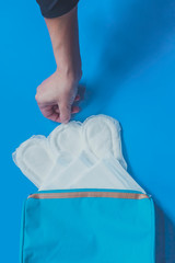 Young women taking sanitary pads inside of her cosmetic bag on blue background