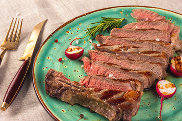 Juicy medium rare beef steak slices on ceramic plate with herbs spices and salt.