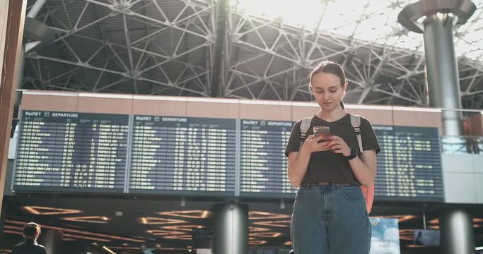 A young woman at the airport with a smartphone near the scoreboard-departures
