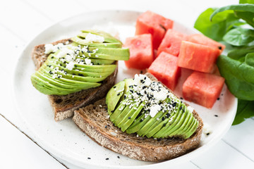 Sliced avocado with soft white cheese on toast served with watermelon cubes. Healthy summer breakfast or lunch