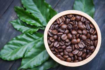 Roasted coffee beans on wooden bowl with green coffee leaf on dark background