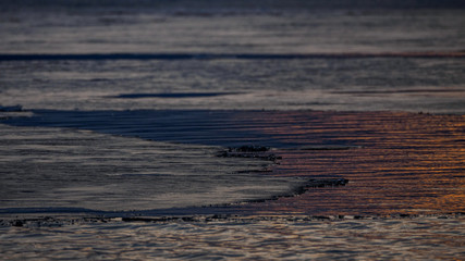 spring ice melts on the lake. reflection of sunset in thawed patches on water. Dramatic scene of natural background. landscape in the evening on the lake.