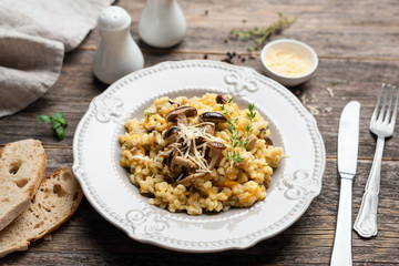 Barley mushroom risotto on plate, rustic wooden table background