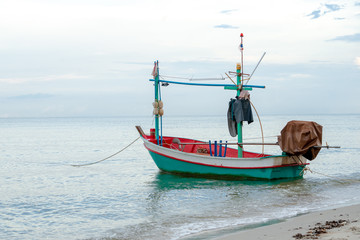 Small traditional fishing boat floating in the sea at coast with calm surface on ocean and clouded sky