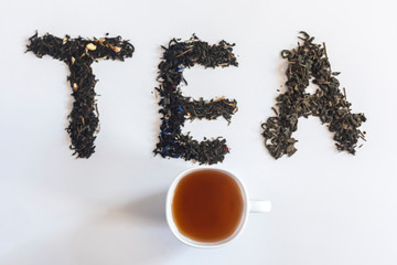 The word tea made with dry tea leafs and a cup of black tea