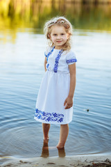 portrait of a little girl who stands in water in a white dress. beach in summer.