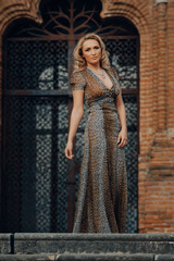 Obraz premium Elegant blonde woman posing against a brick wall wearing a animal print dress.