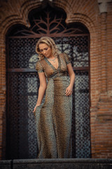 Elegant blonde woman posing against a brick wall wearing a animal print dress.