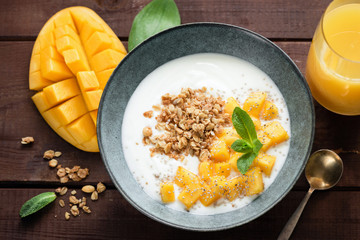Breakfast yogurt bowl with mango and granola on a wooden table background, top view