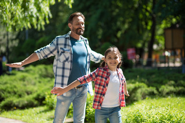 Father Spending Time with Daughter In The Park While Standind Whith Wild Opened Hands And Smiling.