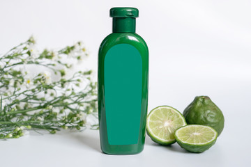 natural products for hair concept. green plastic bottle with blank label contain herbal bergamot shampoo decorate with slide kaffir limes ,kaffir leaf and white flowers on white background