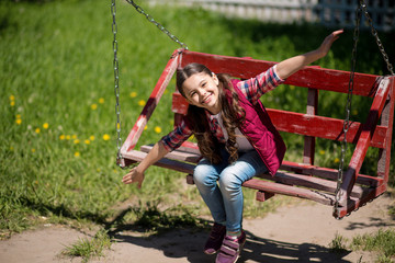 Smiling Little Girl With Long Pigtails Is On The Swing In The Park.