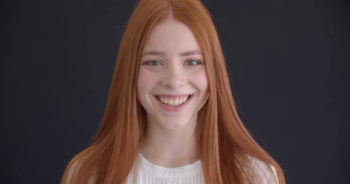 Close-up portrait of beautiful ginger model laughing joyfully into camera on black background.