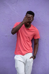 Smiling laughing African American man model posing in empty living coral color t-shirt standing against violet wall background