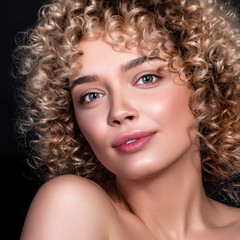 Cute caucasian woman with afro (curls) hairstyle on a dark background. She wears nude make up