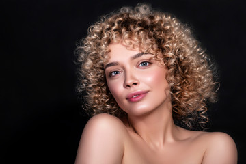 Fototapeta premium Cute caucasian woman with afro (curls) hairstyle on a dark background. She wears nude make up