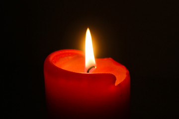 Flame of one white burning brightly wax  candle on the dark black background . Mourning candle. Candle flame