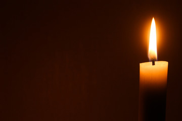 Flame of one white burning brightly wax  candle on the dark black background . Mourning candle. Candle flame