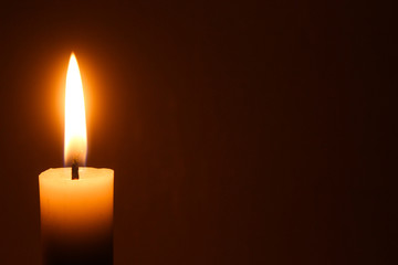 Flame of one white burning brightly wax  candle on the dark black background . Mourning candle. Candle flame