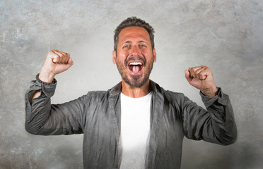 portrait of young happy and attractive Caucasian man gesturing with fist raising arms in victory and success sign smiling cheerful excited feeling strong emotion