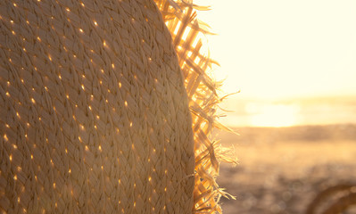 Fragment of a straw hat in sunset light on the beach. Vacation theme concept. Summer holiday background