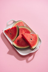 Fresh sliced watermelon in white dish on pink background.