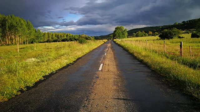 Hermoso paisaje de carretera rural mojada por la lluvia, un atardecer primaveral  soleada con cielo gris tormentoso