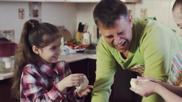 girl with down syndrome and little sister prepare smiling delicious thick dough under father guidance in kitchen