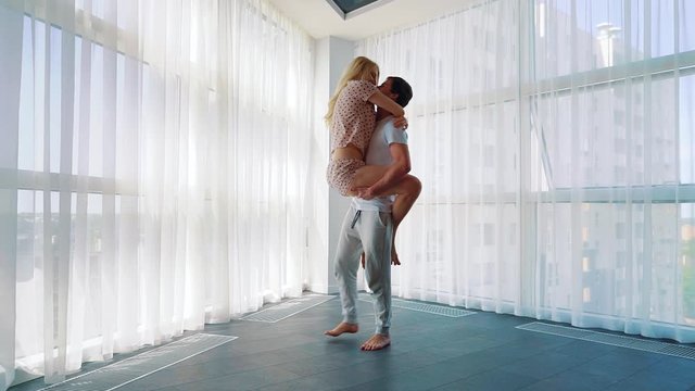 blonde woman jumps into arms of man and he spins around near french window