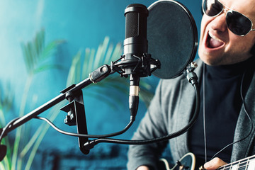 Close up of a man singer sitting on a stool in a headphones with a guitar recording a track in a...