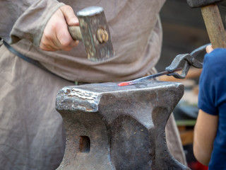 The medieval blacksmith works at forging and heating iron in an ancient forge