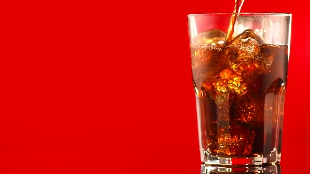 Pouring Coke with ice cubes closeup. Glass of fizzy cola rotated over red background. Slow motion 4K UHD video footage. 3840X2160
