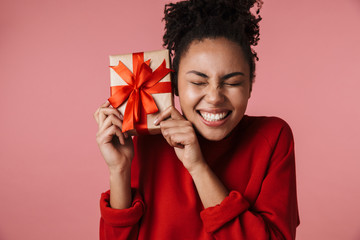 Amazing happy excited young african woman posing isolated over pink wall background holding present...